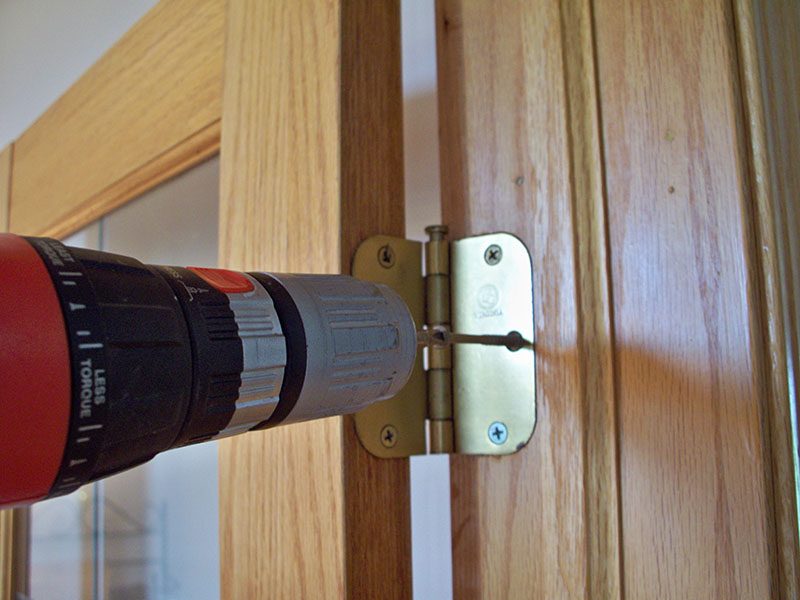 Drill beside a hinge on a wood door